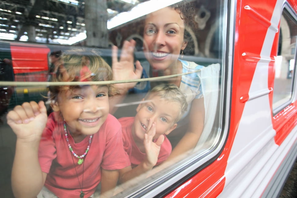 Mutter mit zwei Kindern in einem Zugwaggon, sie winken durch das Fenster